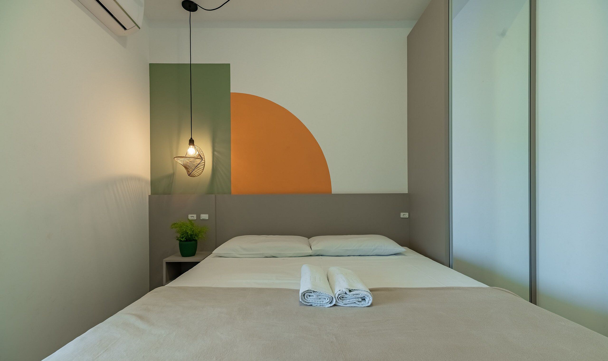 Ein Hotelzimmer mit einem Bett, einer Wandleuchte, einer Topfpflanze und einem großen abstrakten Gemälde.