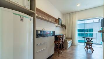 Una cocina moderna con refrigerador, microondas y lavaplatos. Hay dos sillas de madera y una mesita. La habitación tiene un ventanal con vistas a edificios.