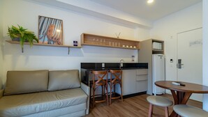 A compact living space with a sofa, a small kitchen area, and a dining table. - Studio w/ Pool 350m From Beach Bombinhas Vec120 (Bombinhas)