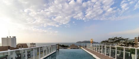 Una piscina infinita en la azotea con vistas despejadas al mar y tierra distante bajo un cielo parcialmente nublado.
