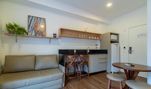 Um espaço de estar compacto com sofá, mesa de jantar para duas pessoas, cozinha compacta e uma porta.