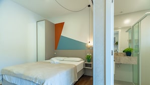 A modern bedroom with a bed, a bedside table with a lamp, and a bathroom with a sink and mirror. - Studio w/ Pool 350m From Beach Bombinhas Vec120 (Bombinhas)