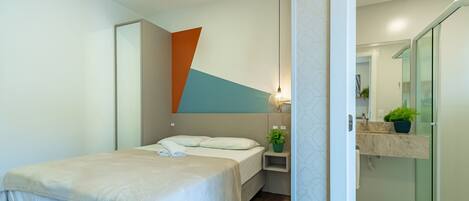Un dormitorio moderno con una cama, una mesita de noche con lámpara, y un baño con lavabo y espejo.