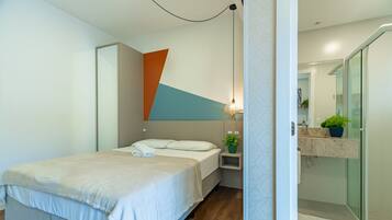 Un dormitorio moderno con cama, mesita de noche y baño con lavamanos y espejo.