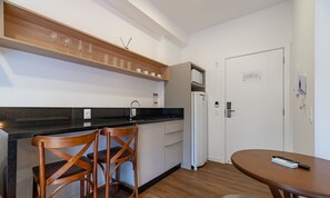 A compact kitchen with a black countertop, wooden chairs, a white refrigerator, and a small dining table. - Studio w/ Pool 350m From Beach Bombinhas Vec120 (Bombinhas)