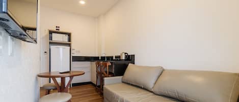 A compact kitchenette with a refrigerator, microwave, and coffee maker. There is a small dining table with two chairs and a sofa in the living area.