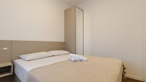 A single bed with white bedding and a beige throw blanket, a nightstand with a power outlet, and a vertical mirror on the wall. - Studio 350m From Beach Bombinhas Vec213 (Bombinhas)