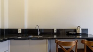 A kitchen with a black countertop, a stainless steel sink, and a kettle. There are two wooden chairs and a white cabinet below the countertop. - Studio 350m From Beach Bombinhas Vec213 (Bombinhas)