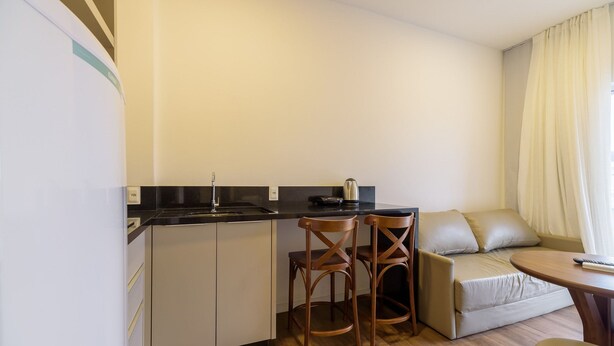 A compact kitchenette with a sink, two wooden chairs, a small table, and a sofa. - Studio 350m From Beach Bombinhas Vec213 (Bombinhas)