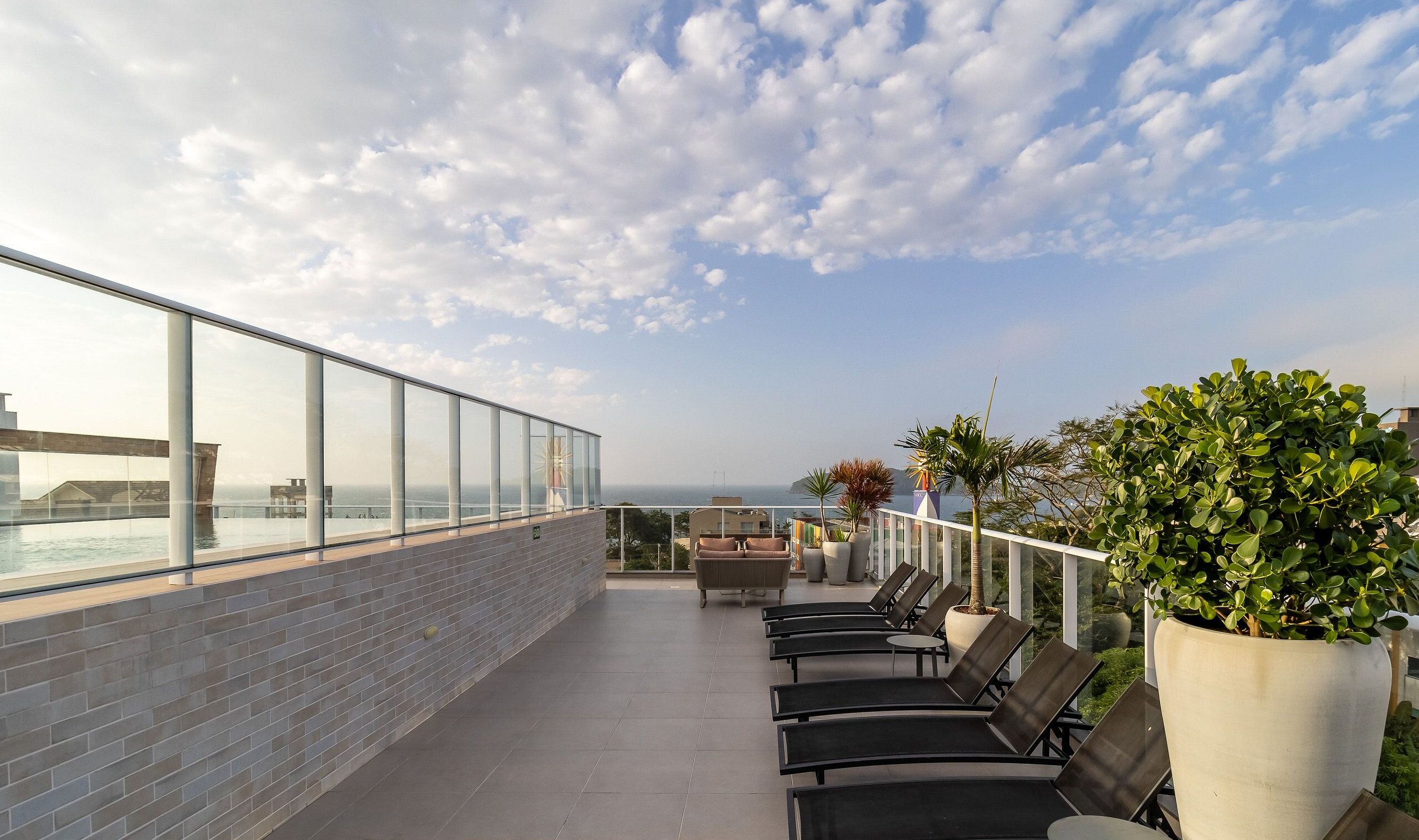 Eine Dachterrasse mit Glasgeländer, Liegestühlen, Topfpflanzen und Blick auf den Ozean.