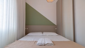Et hotelværelse med en seng, to puder, et sammenfoldet håndklæde og et geometrisk vægdesign.