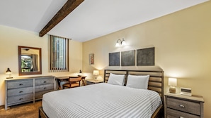 Une chambre d’hôtel avec un grand lit, un bureau, une chaise, une commode et une table de chevet avec une lampe.