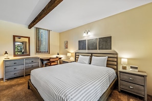 A hotel room with a large bed, a desk, a chair, a dresser, and a nightstand with a lamp. - Mountain Comfort at Ski Ranch 103 – Easy Access to Slopes & Town! (Steamboat Springs)