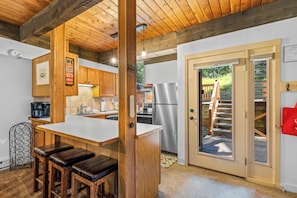A kitchen with wooden cabinets, a stainless steel refrigerator, and a bar area with stools. - Cozy 1BR Ski Stay | Fireplace & Winter Shuttle (Steamboat Springs)