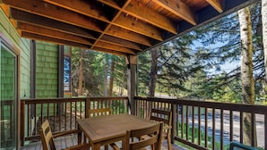 Une terrasse en bois, agrémentée d’une table et de chaises, entourée d’une rambarde et offrant une vue sur une zone boisée.