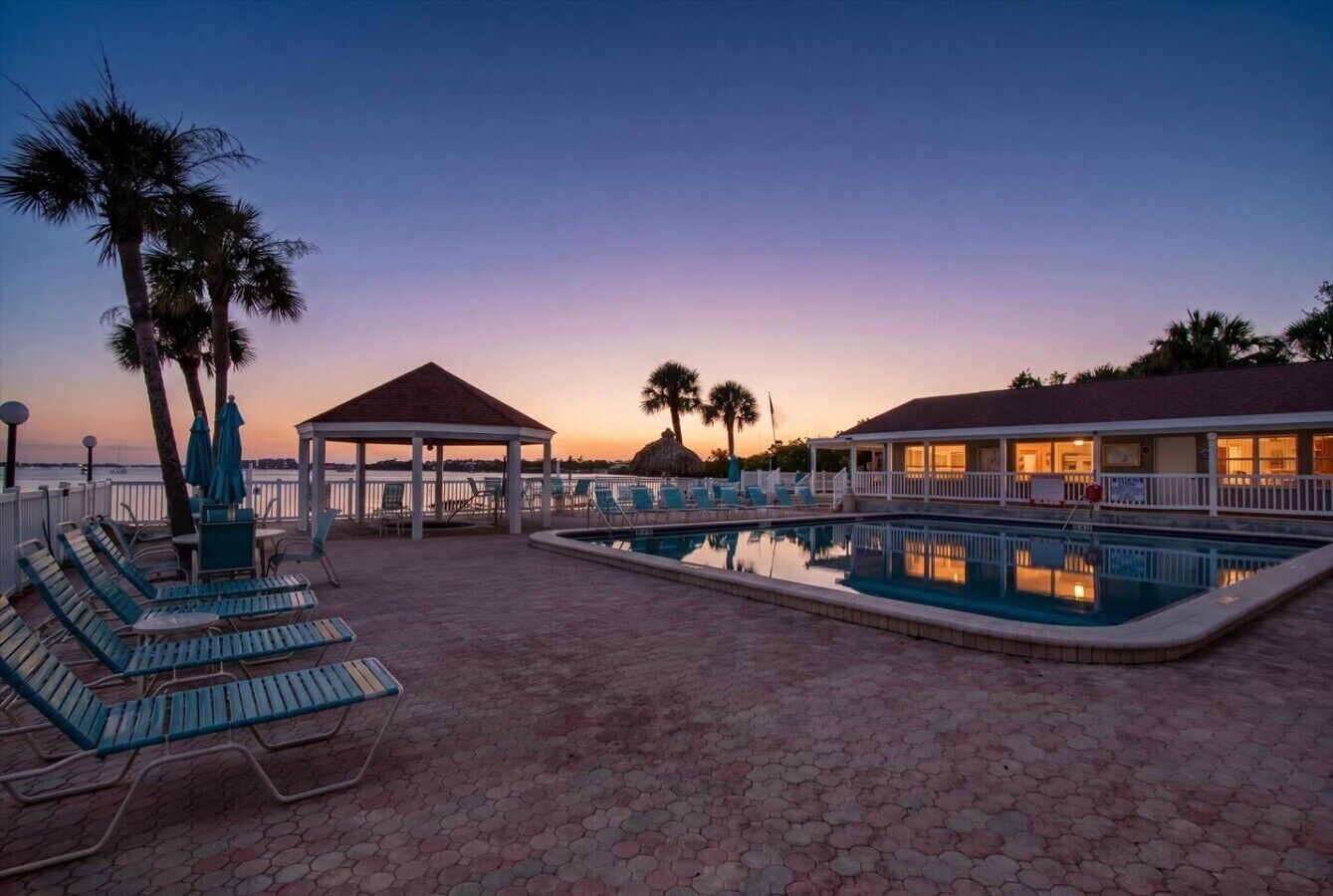A pool area with lounge chairs, a gazebo, and a building with a covered patio.