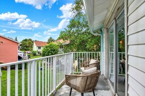 Ein Balkon mit weißer Reling, einem Korbstuhl und einem Kissen.