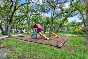 Ein Spielplatz mit einer Spielhaus mit rotem Dach und einer Rutsche in Gelb.