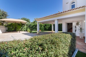A covered outdoor area with a gravel path, white columns, and a white building with a tiled roof. - Villa 'Cadi' with Sea View, Wi-Fi and Air Conditioning (Albufeira)