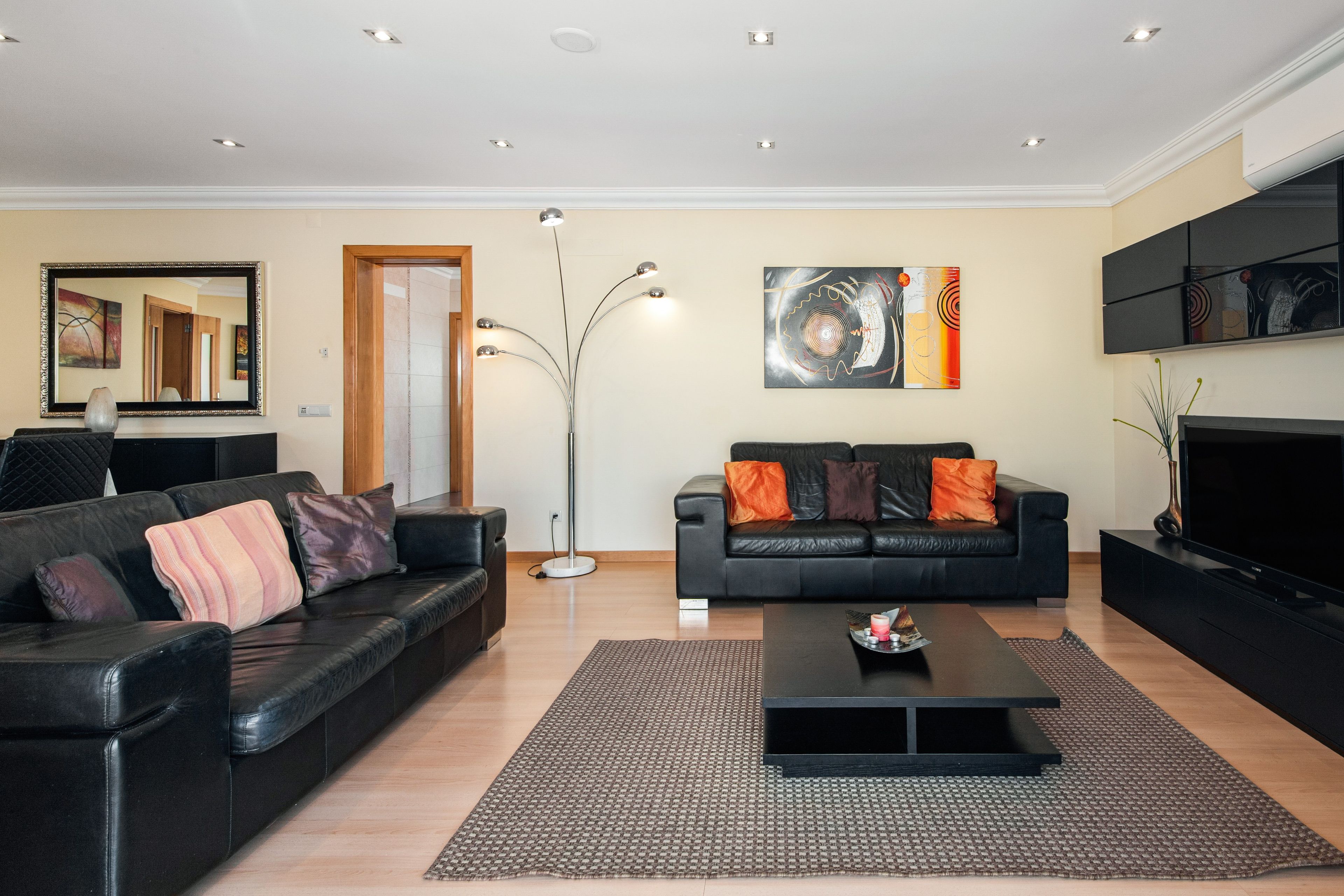 A modern living room with a black leather sofa, a coffee table, and a floor lamp.