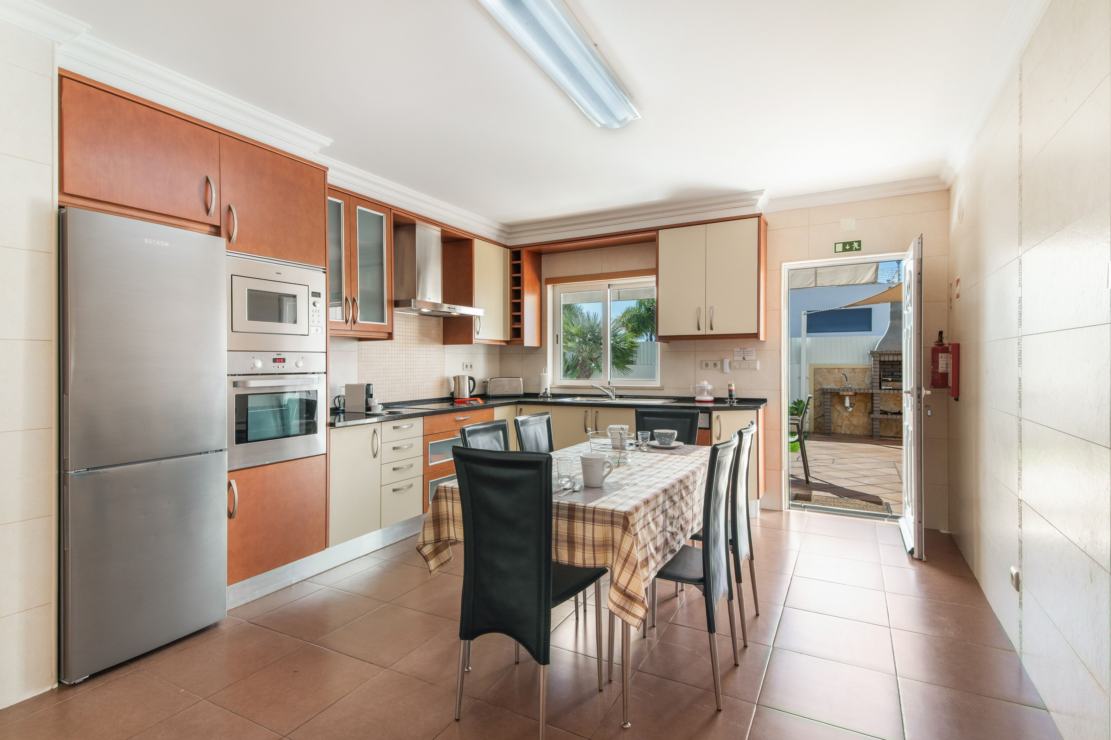 A modern kitchen with stainless steel appliances, a dining area with a table set for two, and a view of the outside through a glass door.