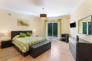 A modern bedroom with a bed, bedside tables, a bench, a desk, a TV, and a sliding glass door leading to a balcony. - Villa 'Cadi' with Sea View, Wi-Fi and Air Conditioning (Albufeira)
