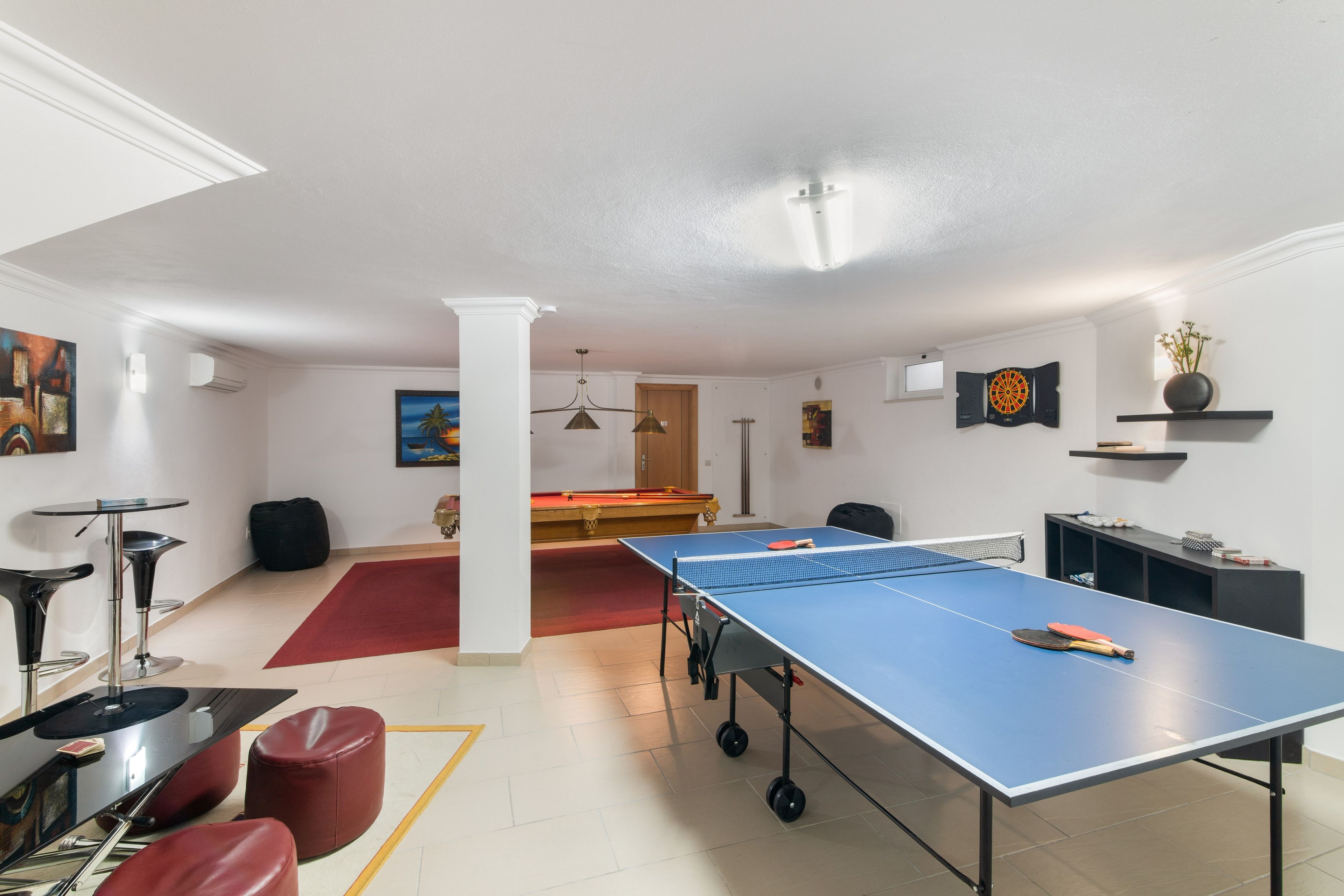 Et rum med et ping pong bord, et billardbord og en dartskive. Der er røde stole og et sort bord med en vase på.