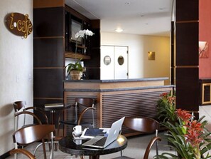 A modern cafe with a laptop on a table, wooden chairs, a refrigerator, and a potted plant. - Bright Room | Near São Paulo Business Hub | Close to Jardim Botânico (São Paulo)