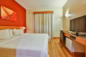 A hotel room with a bed, a desk with a television, and a window with curtains. - Bright Room | Near São Paulo Business Hub | Close to Jardim Botânico (São Paulo)