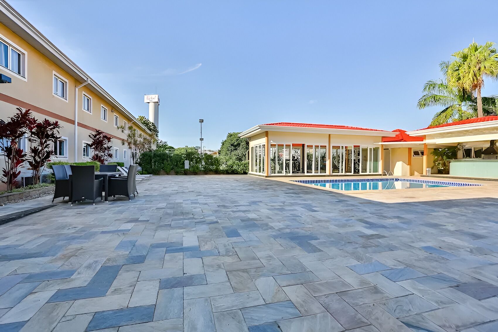 Ampla área externa com piscina, assentos e um edifício com telhado vermelho.