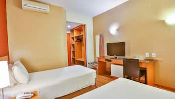 A hotel room with two single beds, a desk with a chair, a television, and a wardrobe.