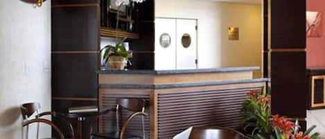 A modern cafe with a laptop on a table, wooden chairs, a refrigerator, and a potted plant.