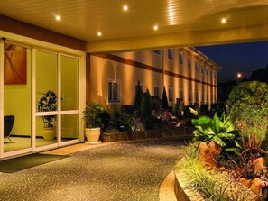 A hotel entrance with a paved pathway, potted plants, and a building with large windows and a balcony. - Family-Friendly Stay | Free Breakfast & Pool | Near Jardim Botânico (São Paulo)