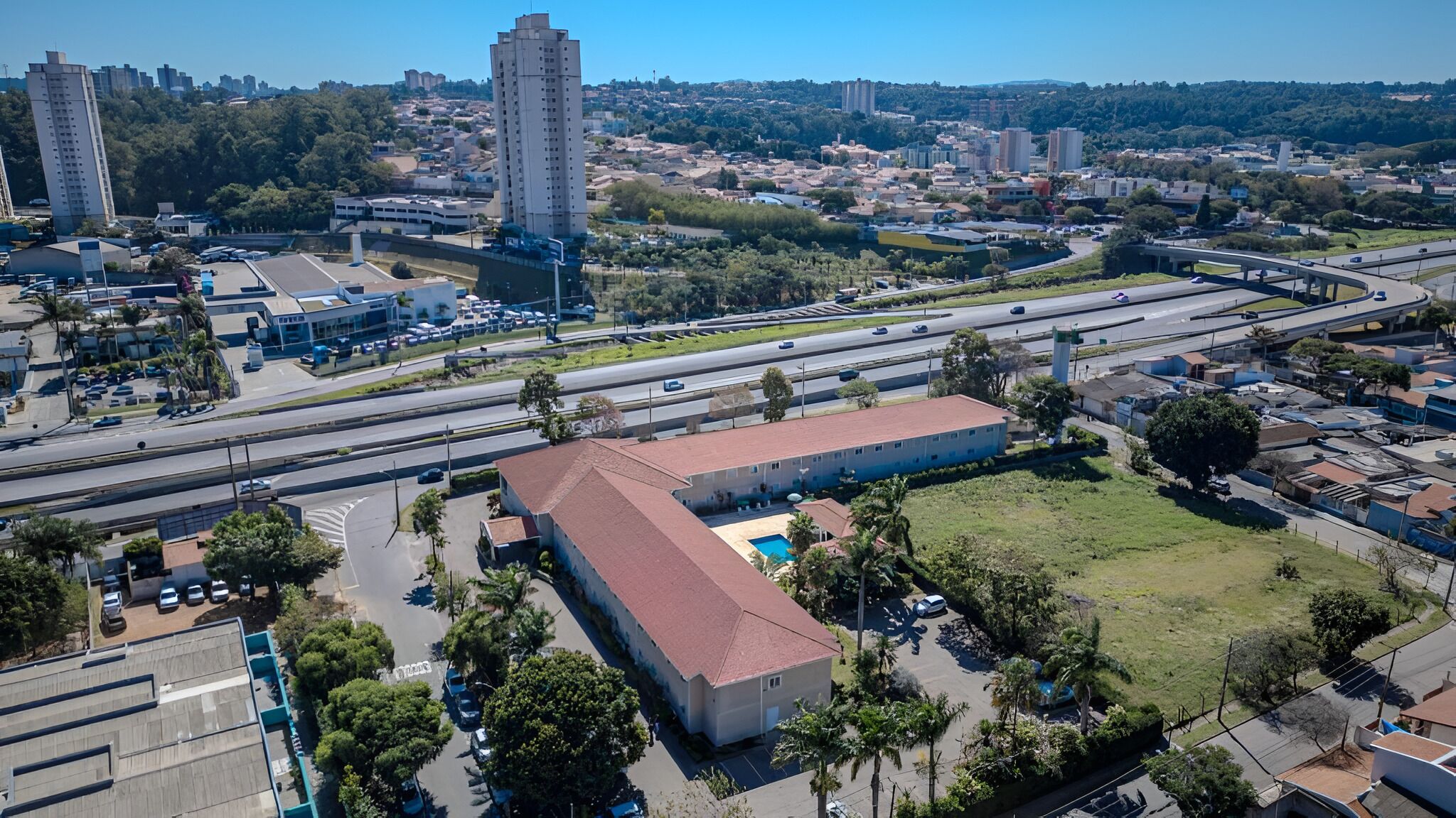 Luchtbeeld van een stadsgezicht met een opvallend gebouw met een rood dak, omringd door groen en een parkeerplaats.