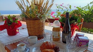 Ein Tisch gedeckt mit einer Weinflasche, einem Wasserglas, einer Packung Bonomelli-Fruchtsaft, einem Croissant, einem Gebäckstück und einer Kaffeetasse.