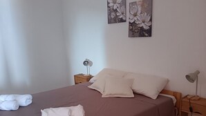 Ein ordentlich bezogenes Bett mit Kissen und Handtüchern, ein Nachttisch mit einer Lampe sowie zwei an der Wand hängende Blumenbilder.
