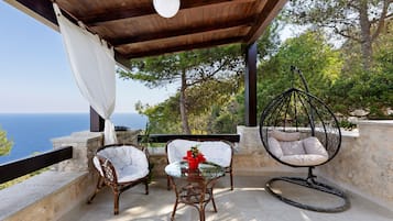 A covered outdoor seating area with wicker chairs and a hanging chair, overlooking a body of water.