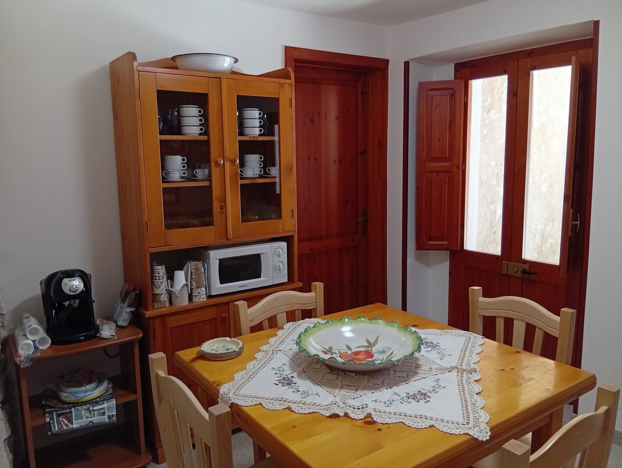 Un coin repas comprenant une table en bois, des chaises, un four à micro-ondes et un meuble contenant des tasses.