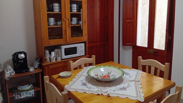 Ein Essbereich mit einem Holztisch, Stühlen, einer Mikrowelle und einem Schrank mit Tassen.