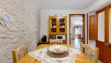 A dining area with a wooden table, chairs, a decorative plate, a coffee machine, and a cabinet with glass doors.