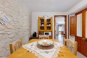 A dining area with a wooden table, chairs, a decorative plate, a coffee machine, and a cabinet with glass doors.