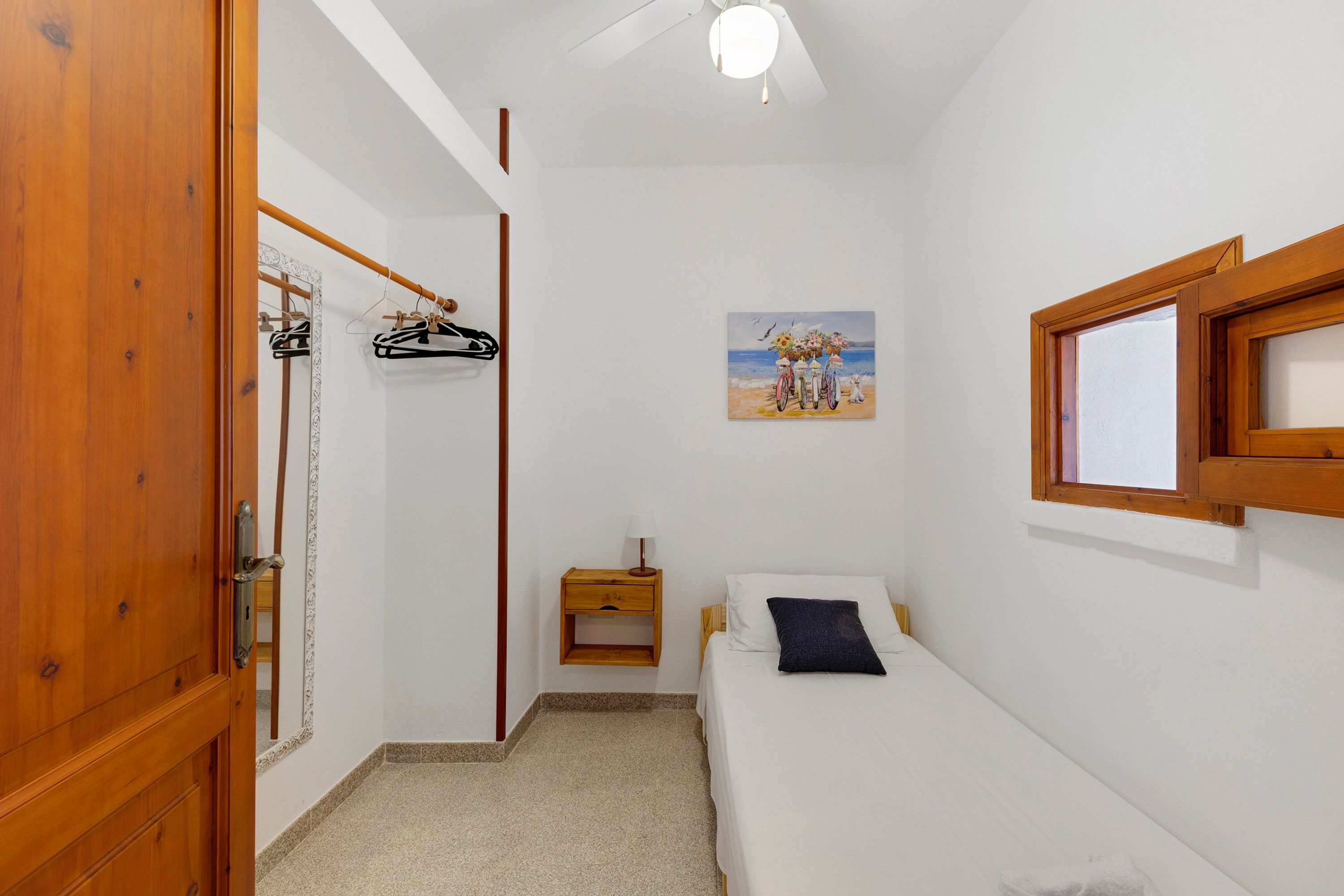 A bedroom with a bed, a nightstand, a hanging coat rack, a painting, and a window.