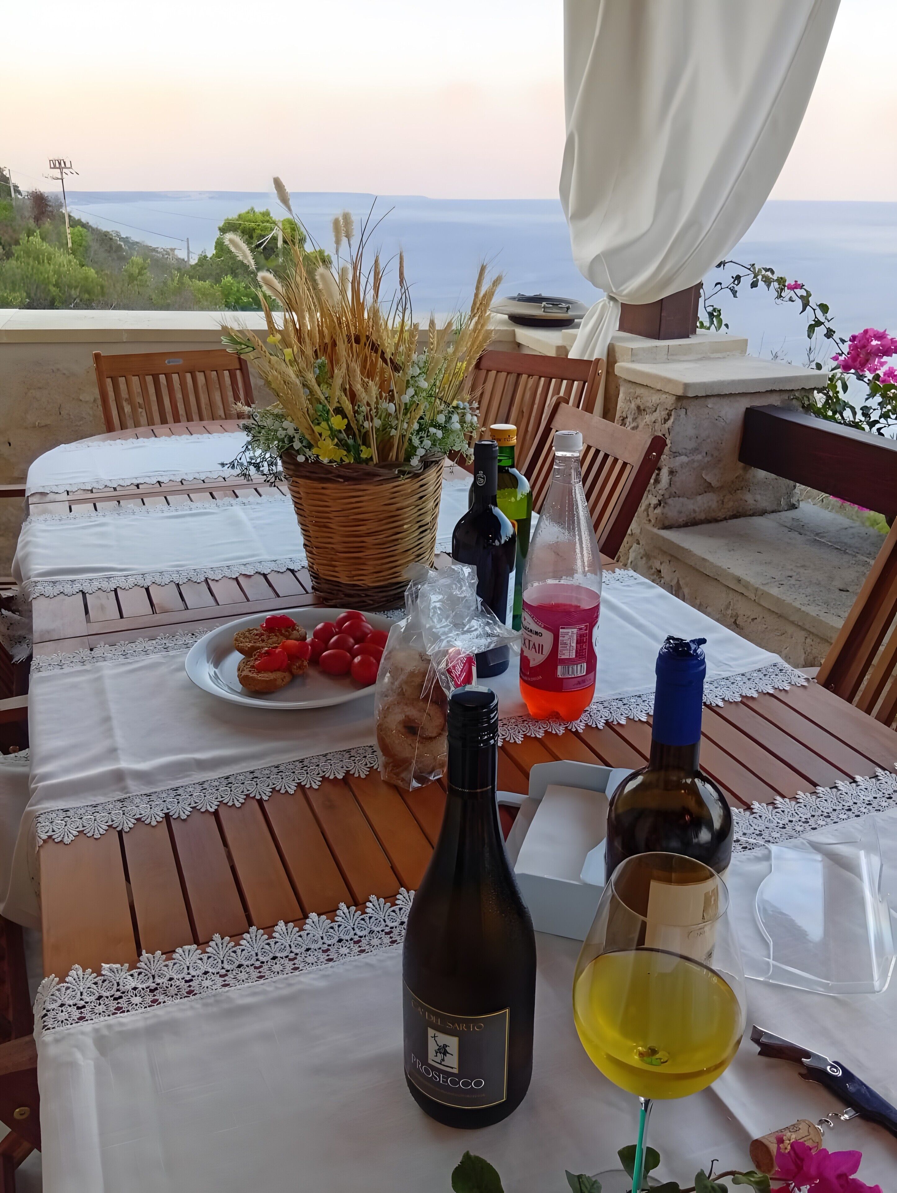 Une table dressée à l’extérieur, avec une bouteille de Prosecco, un verre de vin et une assiette de nourriture.