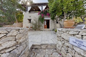 A stone-walled entrance with a wooden door and steps leading to a villa.