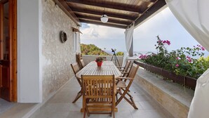 A covered outdoor patio with a wooden table and chairs, a hanging light fixture, and a view of the sea.