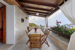 A covered outdoor patio with a wooden table and chairs, a hanging light fixture, and a view of the sea.
