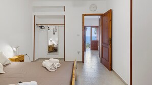 A bedroom with a bed, a bedside table, a lamp, a mirror, and a view of the sea through an open door.