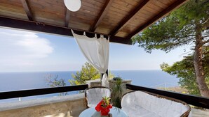 A balcony with wicker furniture, a glass table, and a view of the sea.