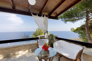 A balcony with wicker furniture, a glass table, and a view of the sea.