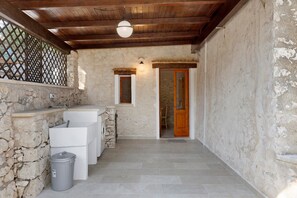 A stone-walled bathroom with a sink, a mirror, and a wooden door.